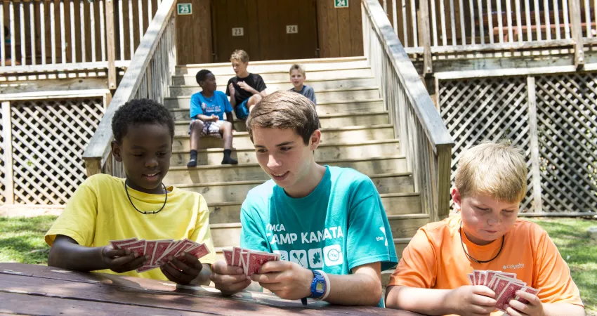 Two boys and counselor playing cards at picnic table